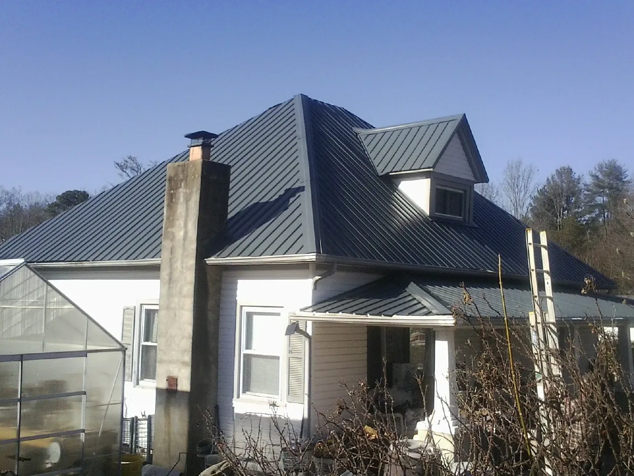 Dark blue standing seam metal roof on a white farmhouse with dormer — Slate & Tile Roof Repair by Roofing Brothers in Meservey