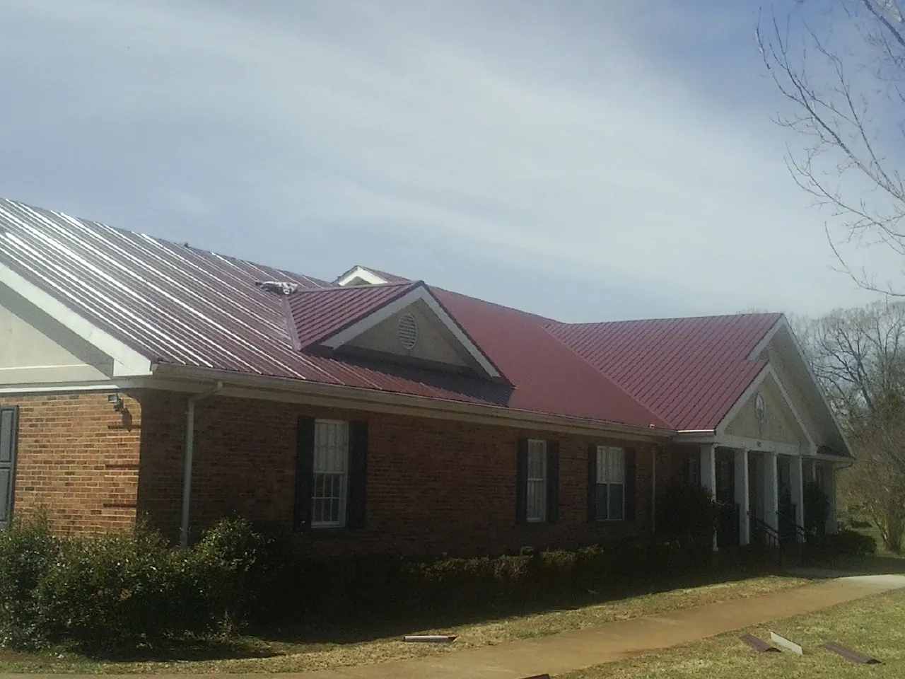 Red metal roof with gabled entries on a long brick building, from a Hail Damage Roof Repair job in Meservey