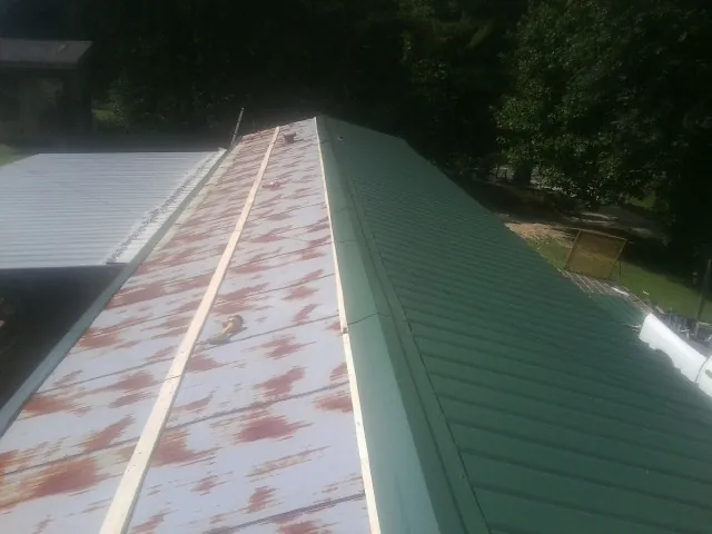 Old rusted panels beside newly installed green metal roofing — Wind Damage Roof Repair by Roofing Brothers in Meservey