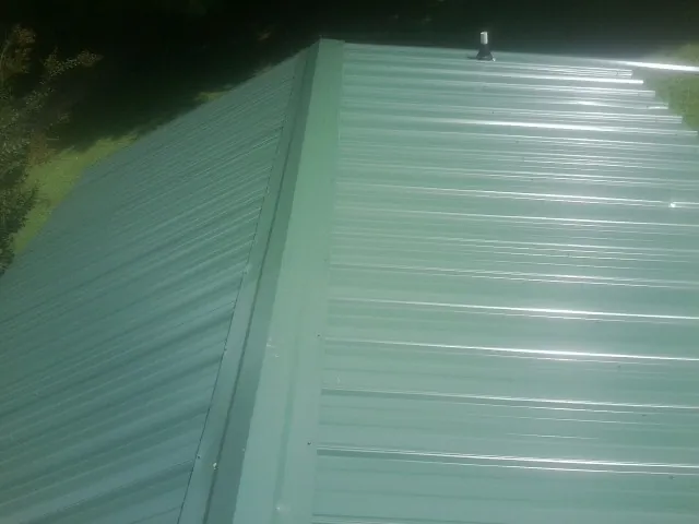 New green metal panels meeting at the ridge of a roof — Flat Roof Repair work by our crew in Meservey