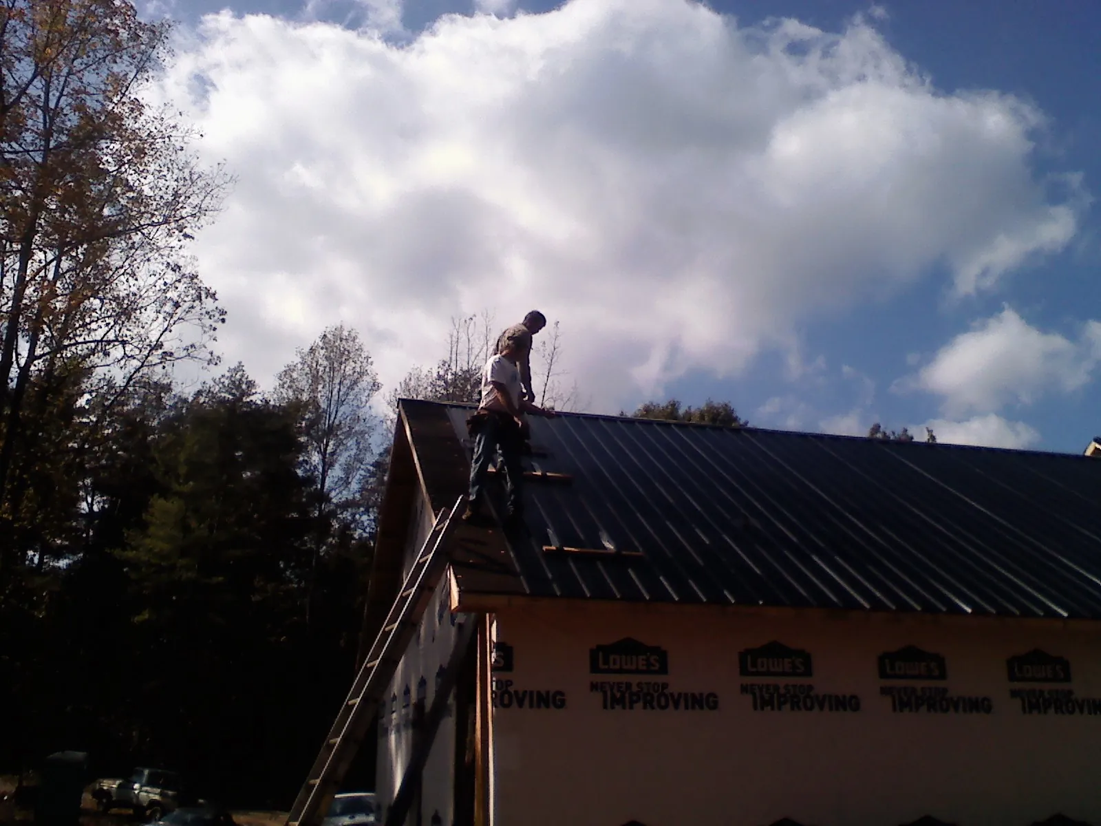 Roofer fastening dark metal panels high against a cloudy sky, from a Roof Inspection job in Meservey