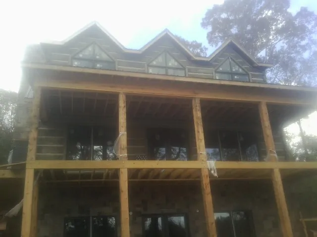Dormers and porch framing on a large log home under construction — Roof Coating work by our crew in Meservey