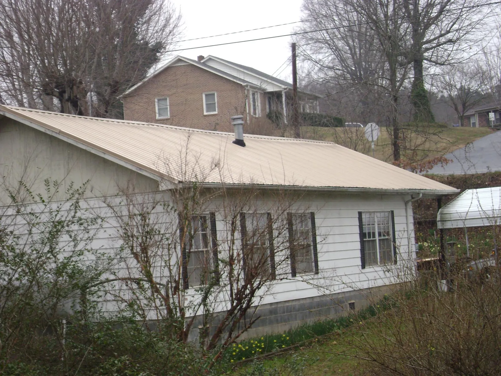 Tan metal roof on a white sided house set into a hillside — Commercial Roofing by Roofing Brothers in Meservey