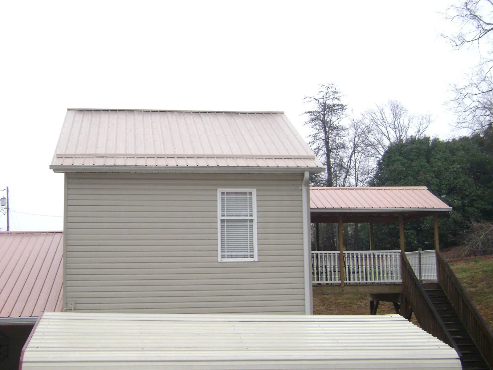 Tan metal roofs on a two story addition and attached porch, from a Roof Replacement job in Meservey