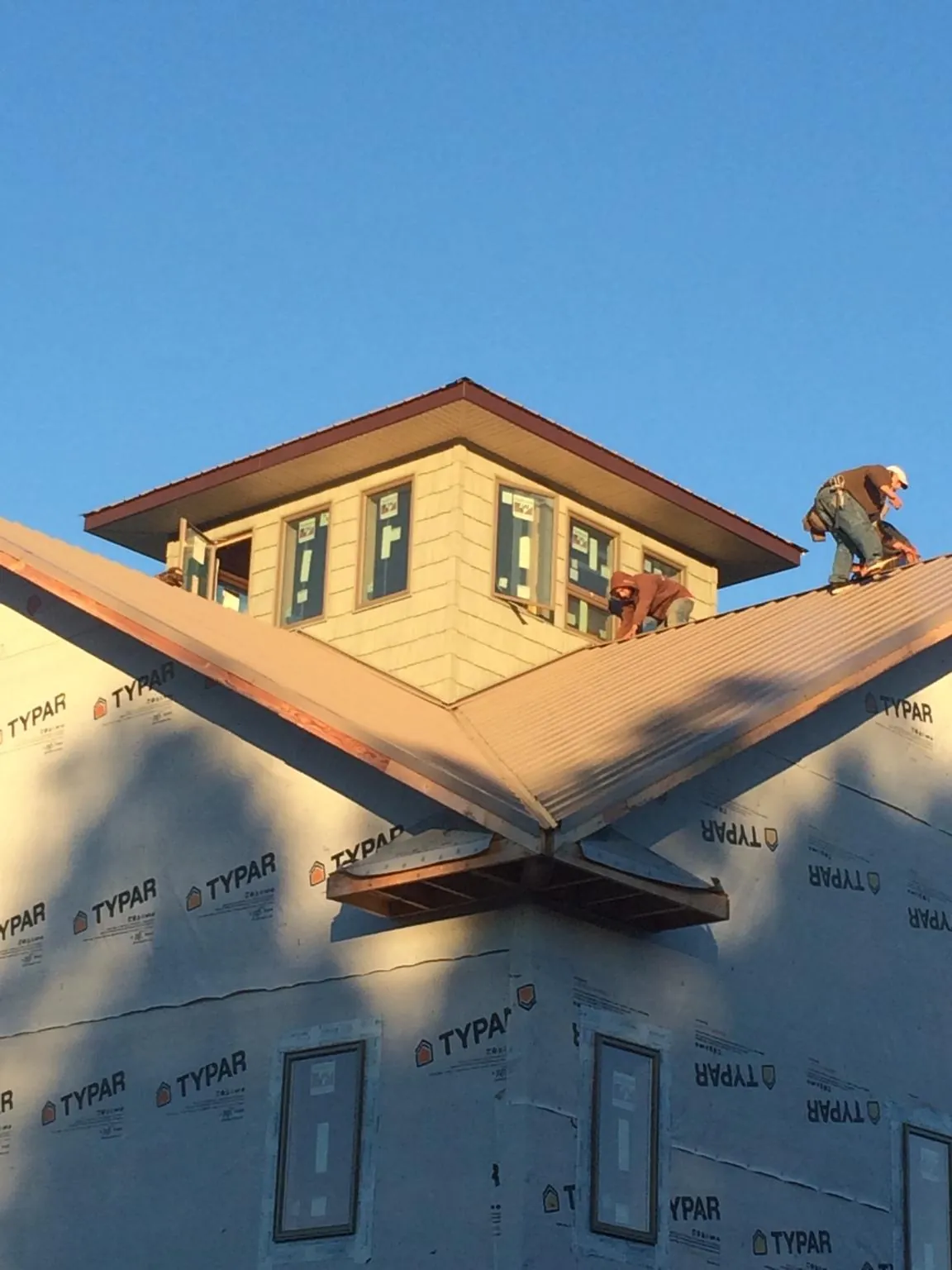 Roofers working around a rooftop cupola on a new metal roof at sunset in Meservey